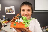 A boy holds up a Lego creation of dinosaurs.