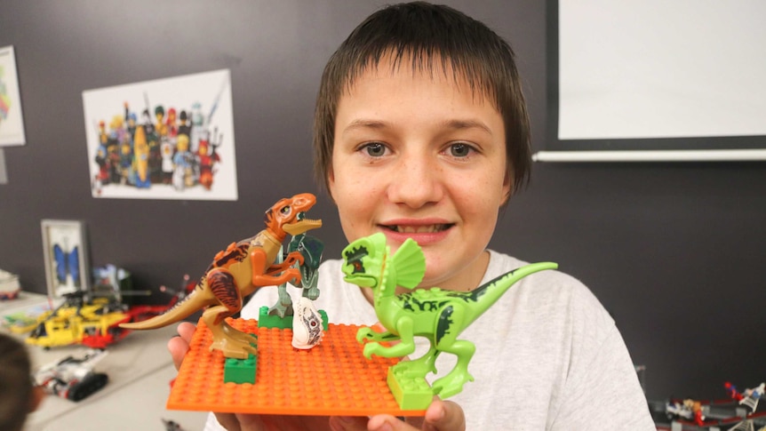 A boy holds up a Lego creation of dinosaurs.
