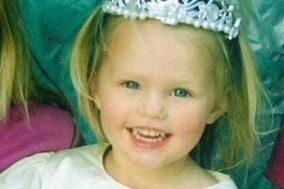 A young girl with blonde hair and a wide smile wearing a tiara