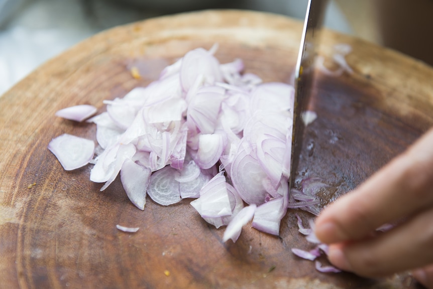 A person slices shallots on a board.