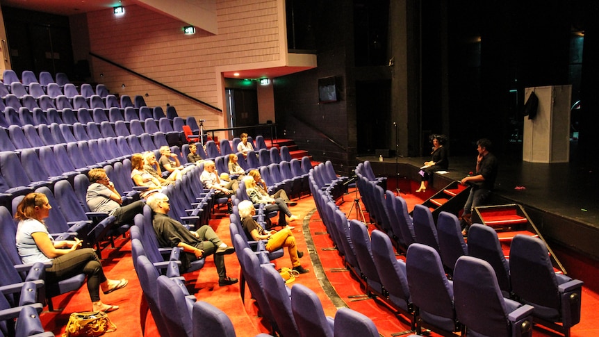 A large theatre with a small number of audience members sitting far apart.