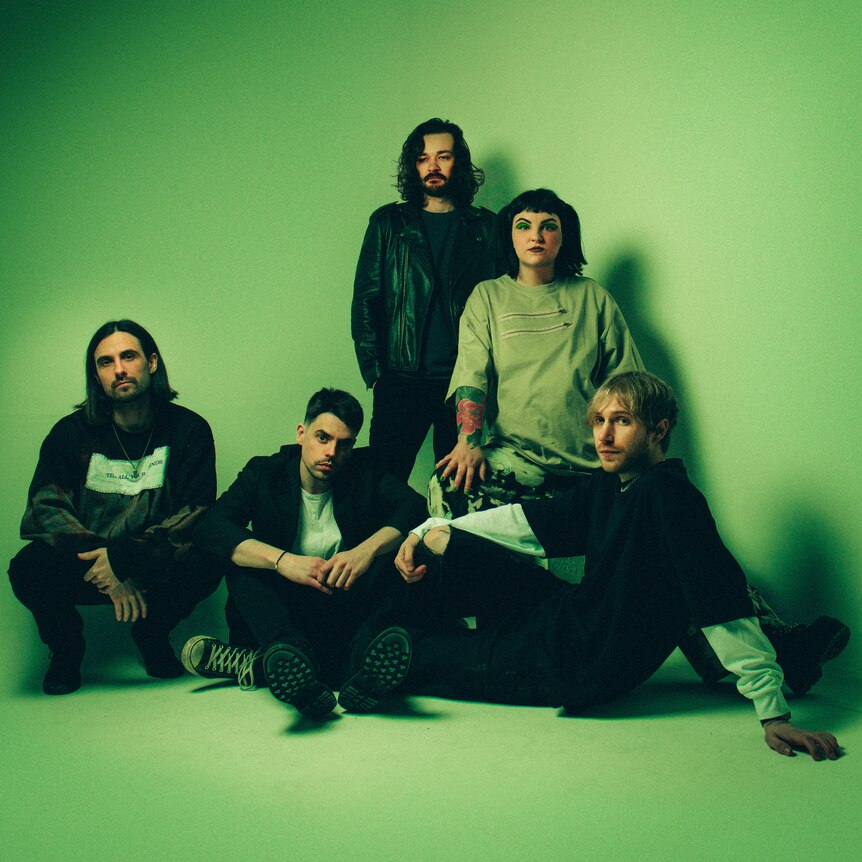 Press photo of UK band Tigress, band members sitting in a green background looking into camera.