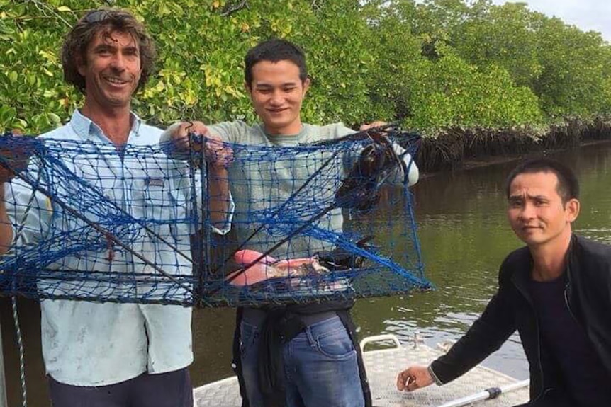 Three men in the back of a fishing boat holding crab pots