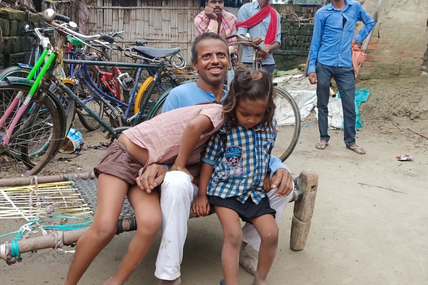 Rampukar sits on a bench with two small children on his lap
