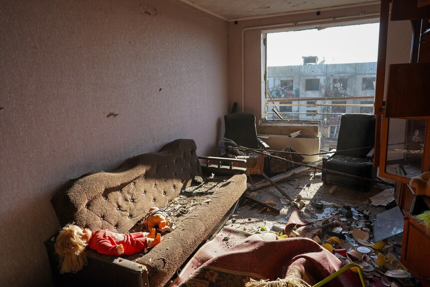 A doll rests on a couch in what appears to be a residential apartment hit by an airstrike