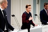 Mette Frederiksen, standing between two men, gestures at a podium she speaks