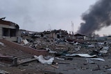 Destroyed remnants of buildings with black smoke coming from the rubble.