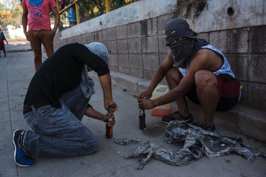 Two men with their faces covered prepare bottles full of petrol.