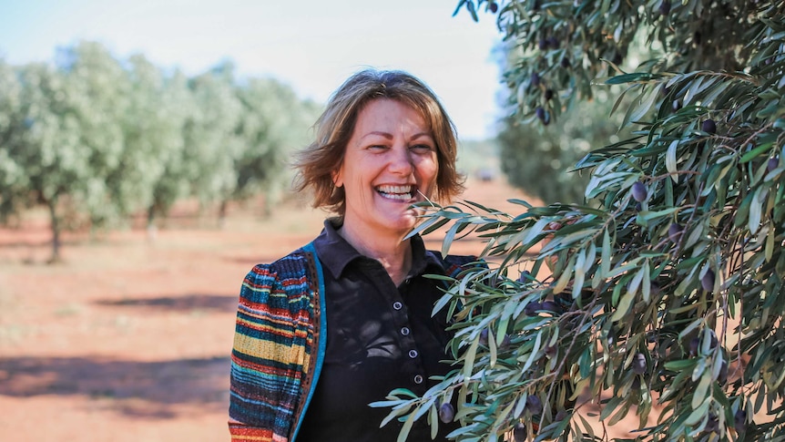 A woman standing beside an olive tree.