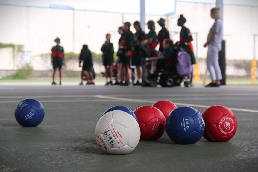 Seven boccia balls with a group of students in the background