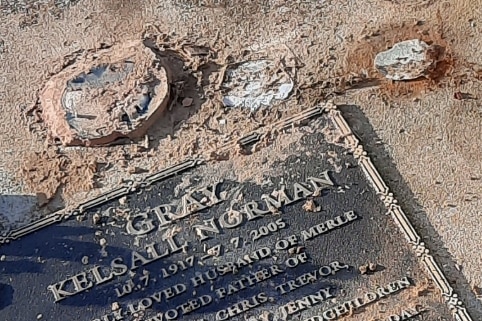 The smashed bases of glass vases on a headstone in a cemetery.