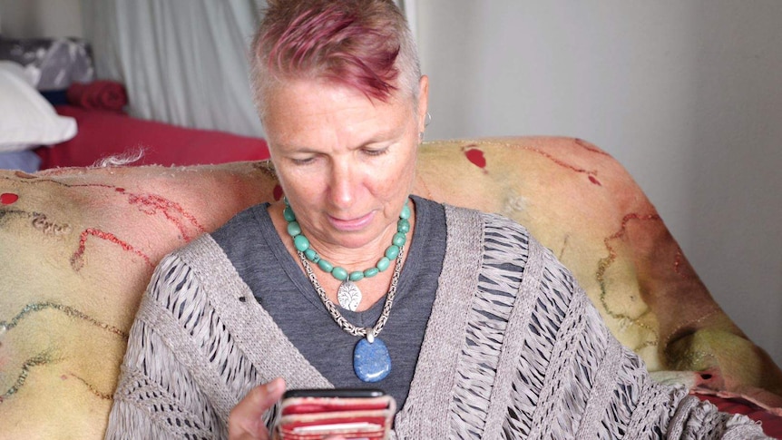 Woman with shaved and pink hair sits on her lounge looking down at her phone.