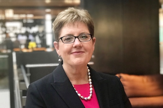 Woman stands in a lobby wearing a jacket.