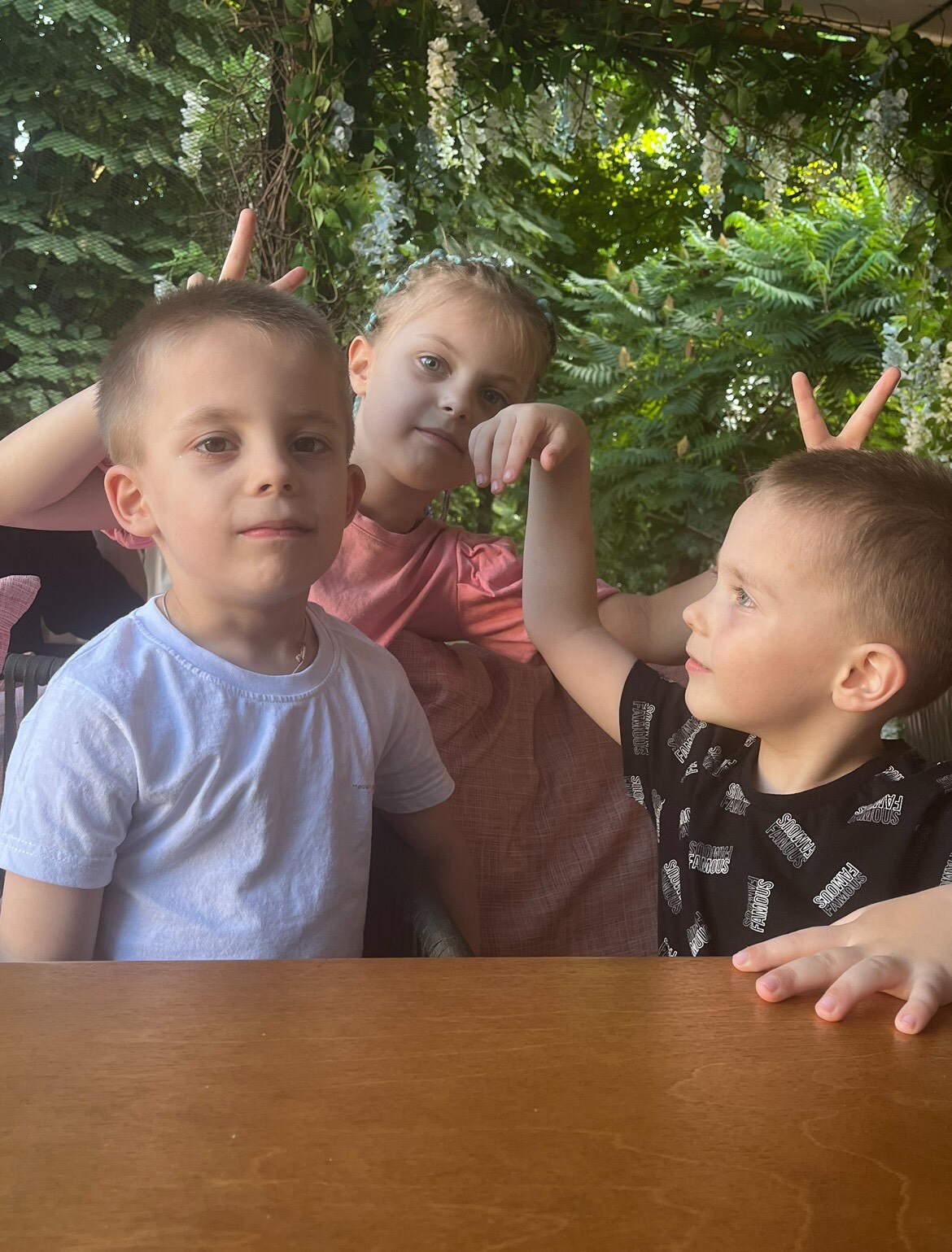 three young children pose for a photo by making gestures behind each other's heads. 