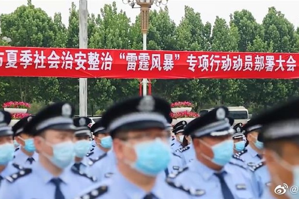 Police in front of banner in Mandarin saying "Public Security Crackdown 'Thunderstorm' launching meeting"