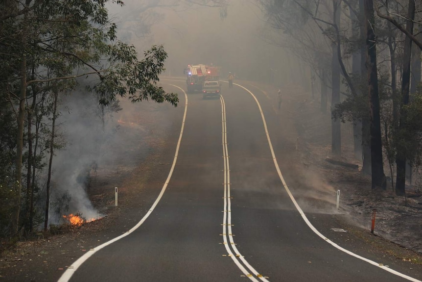 Fire crews on the road amid thick smoke.