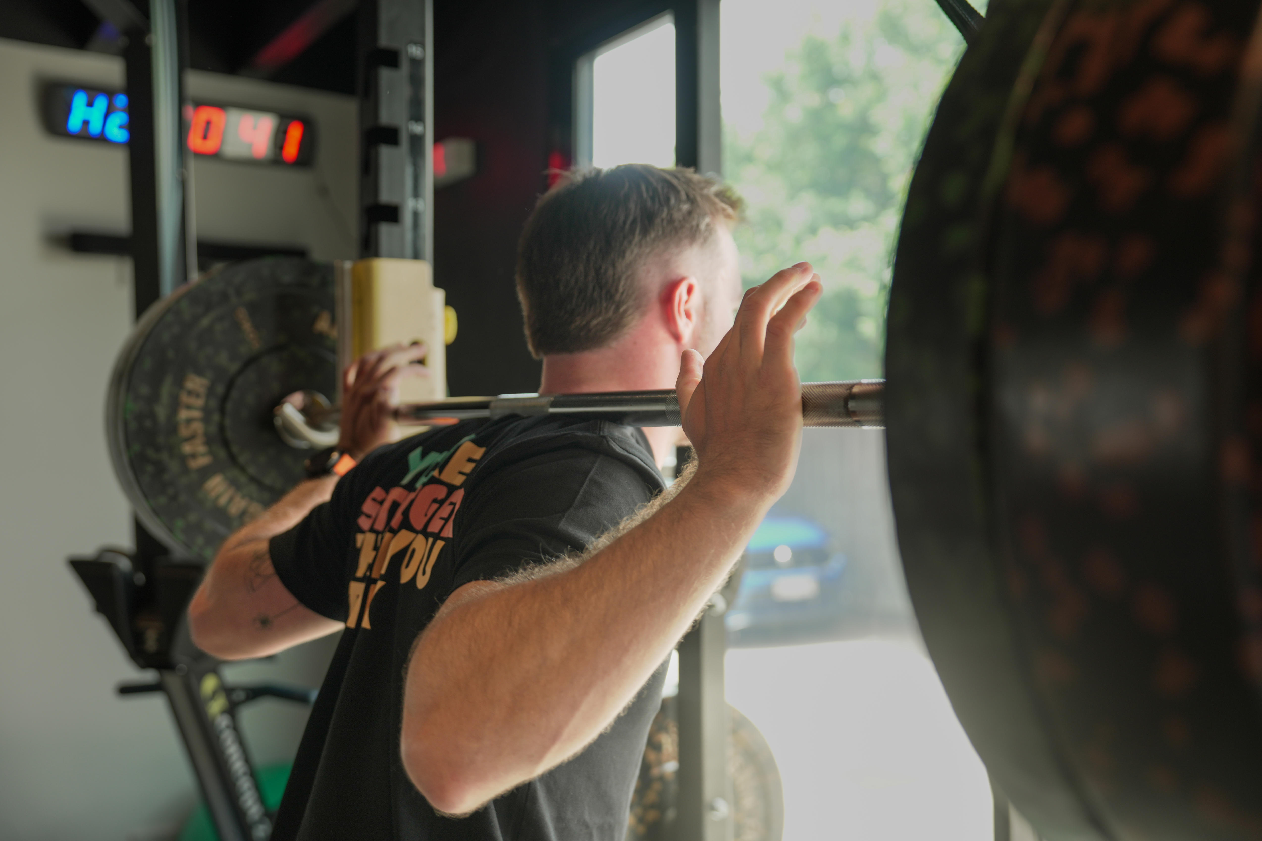 Un hombre con una camiseta negra levantando pesas de espaldas a la cámara