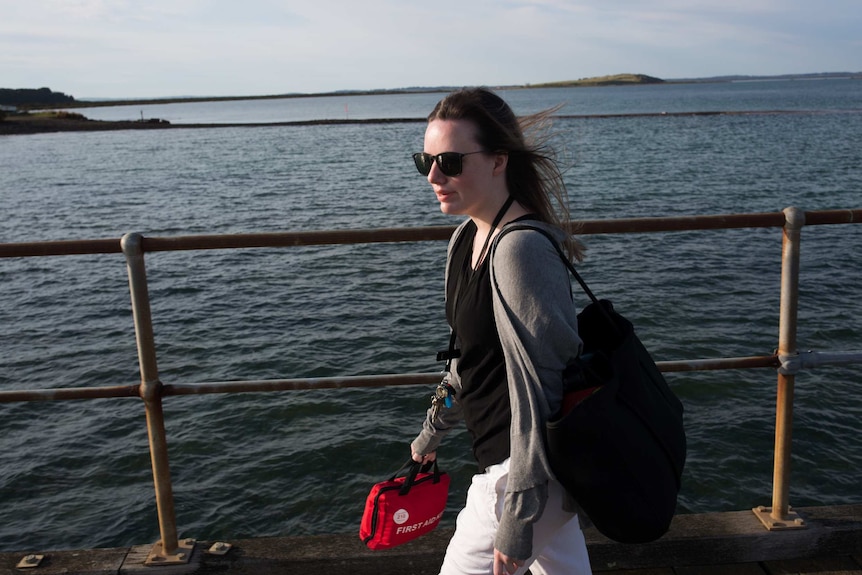 A first aid kit in her hand, teacher Anita Harding strides along a jetty, ocean and an island visible behind her.