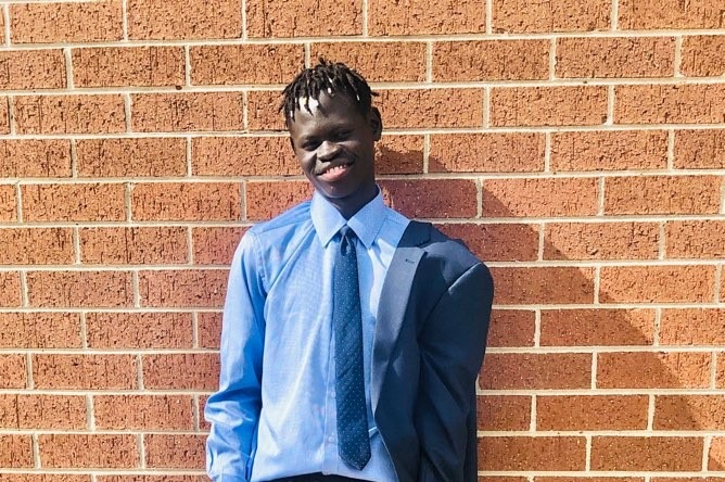 Bol Tong smiles while standing by a brick wall