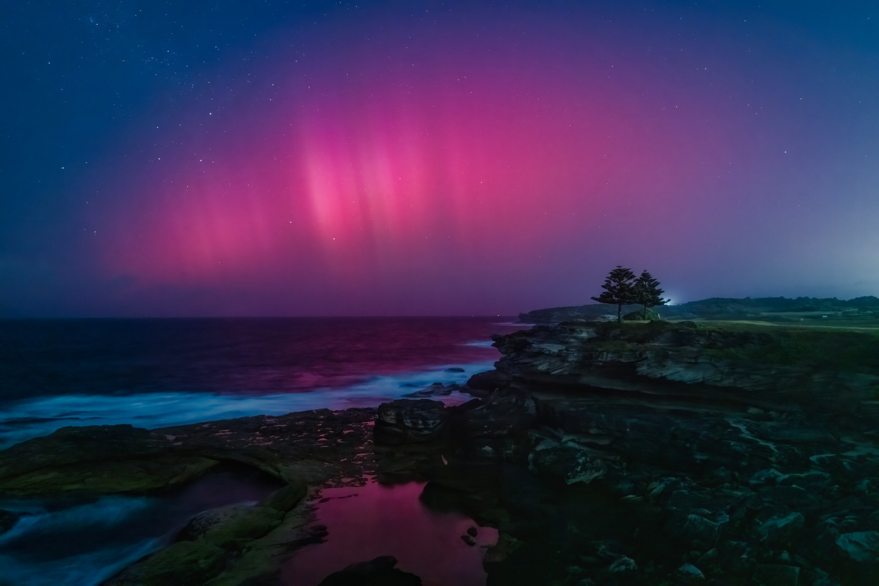 A photo of the ocean with a pink aurora in the night sky