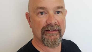 Corporate headshot of a bald, bearded man in a black T-shirt.