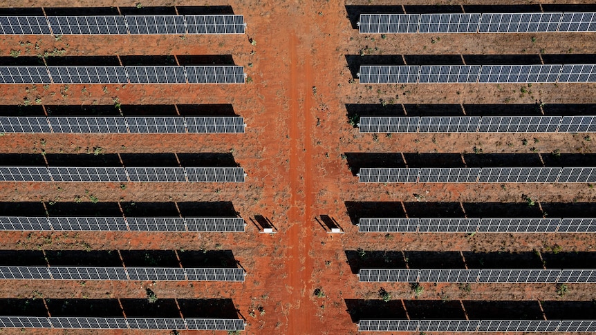 Aerial view of rows of solar panels on red soil from directly above.