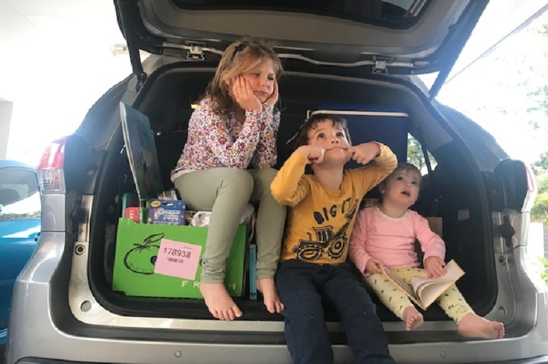 Three children Eloise 5,William 3 and Emily, 1, sit in the back luggage compartment of a car.