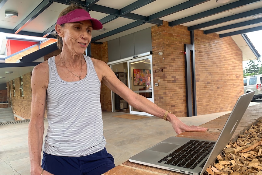 A woman in running gear standing at a laptop outdoors.