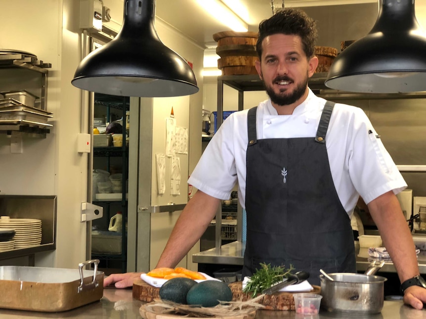 Chef Ash Martin stands in front of this work bench with rosemary and cured egg yolks in front of him.