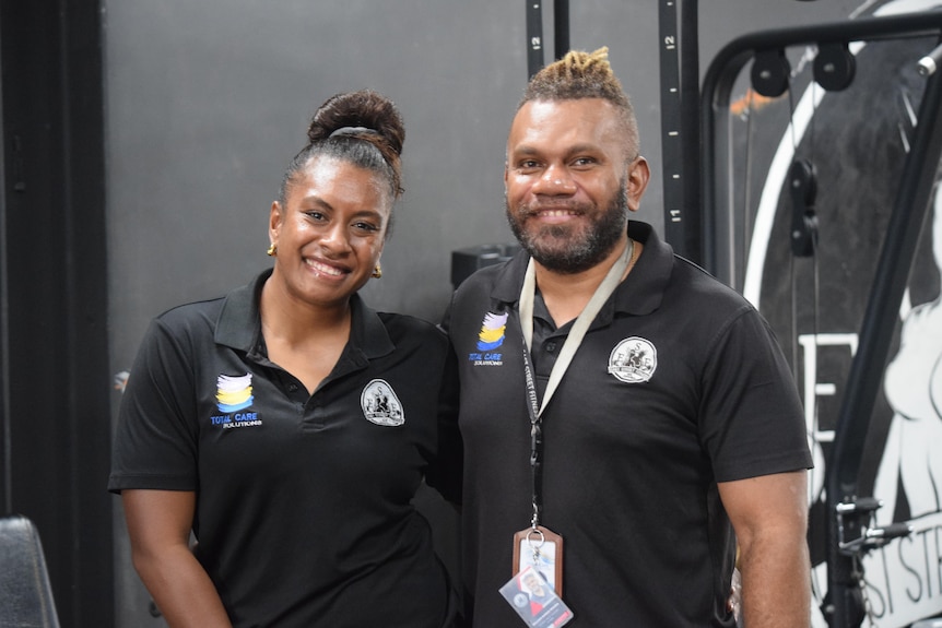 A Papua New Guinean woman and a man, wearing black polo shirts, stand next to each other and smile at the camera.