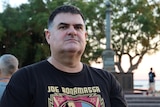 A man wearing a black T-shirt is pictured at the vigil. He has a solemn expression.