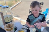 A boy fits a lid to a cup of lemonade at a lemonade stand. 