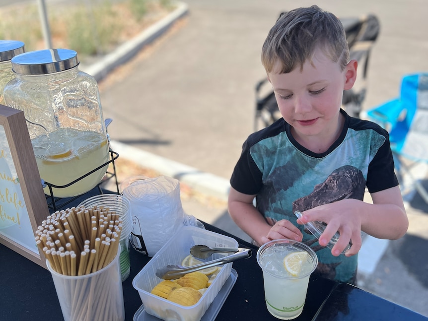 A boy fits a lid to a cup of lemonade at a lemonade stand. 