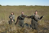 Three people hold a massive python in the Everglades.