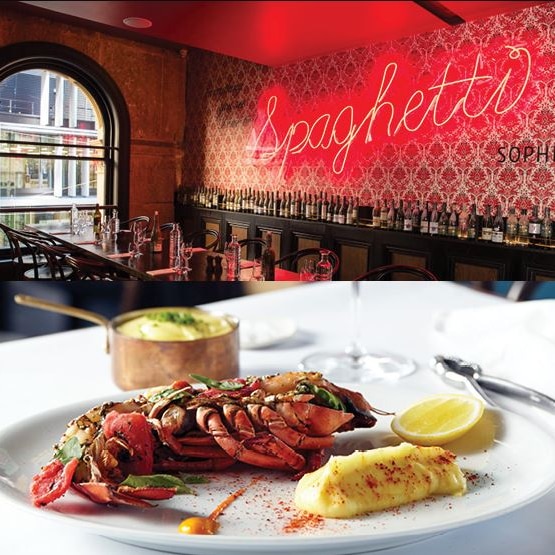 A crustacean on a white plate with a sauce and lemon wedge on a table in front of an empty, set restaurant.