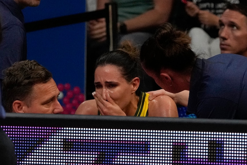 Une basketteuse australienne en détresse est assise sur la touche tandis qu'un entraîneur pose sa main sur son épaule.