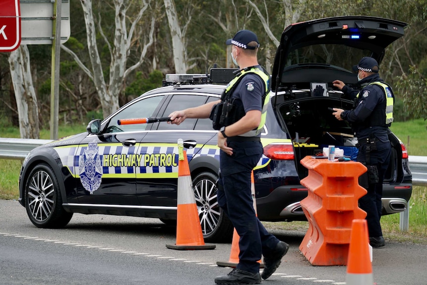 A police officer stands next to a police car directing traffic at a checkpoint.