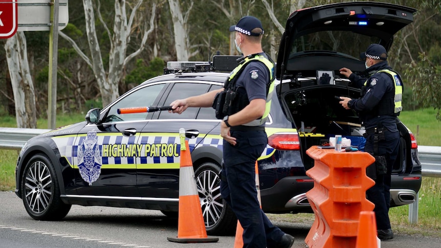 A police officer stands next to a police car directing traffic at a checkpoint.
