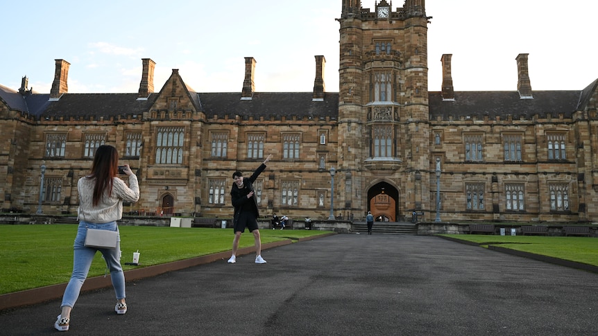 Two Chinese international students take photos in front of the University of Sydney. 