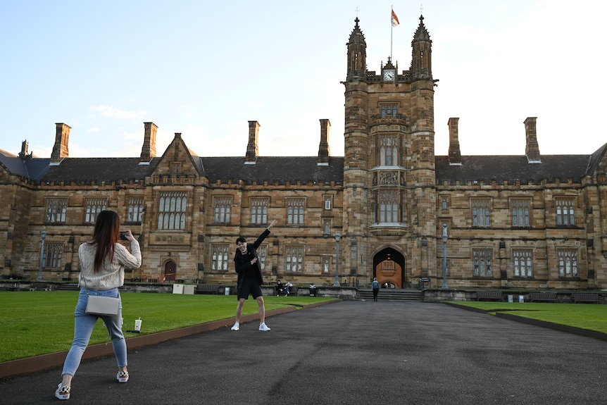 Two Chinese international students take photos in front of the University of Sydney. 