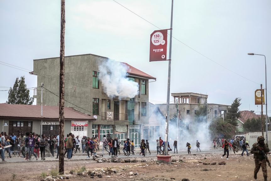 Residents protest against the United Nations peacekeeping force as smoke rises behind them.