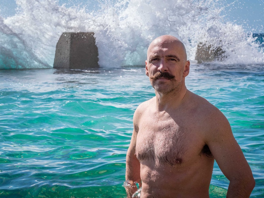 Kenton Webb sporting a large moustache, stands with his hands on his hips, ready to get wet at the Coogee ocean pool