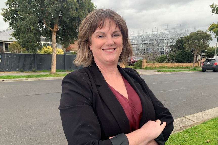 A woman wearing a blazer with her arms crossed, in front of construction.