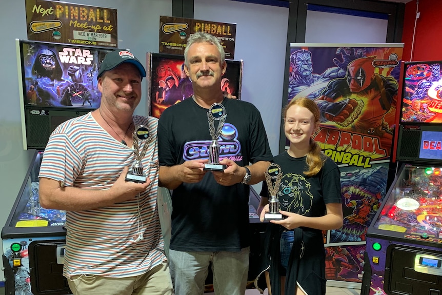 Two men and a teenage girl with pinball trophys