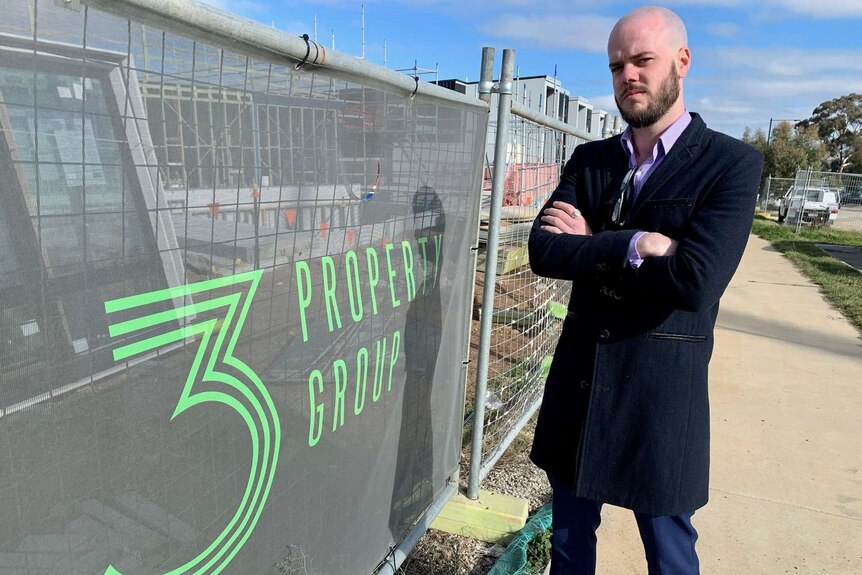 A man stands with his arms folded beside construction hoarding bearing a 3 Property Group logo.