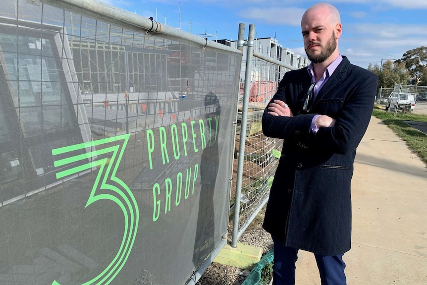 A man stands with his arms folded beside construction hoarding bearing a 3 Property Group logo.