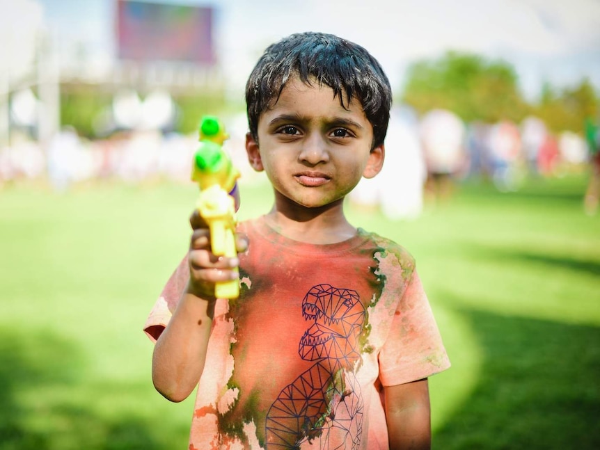A little boy aims a water pistol at the camera during Holi celebrations