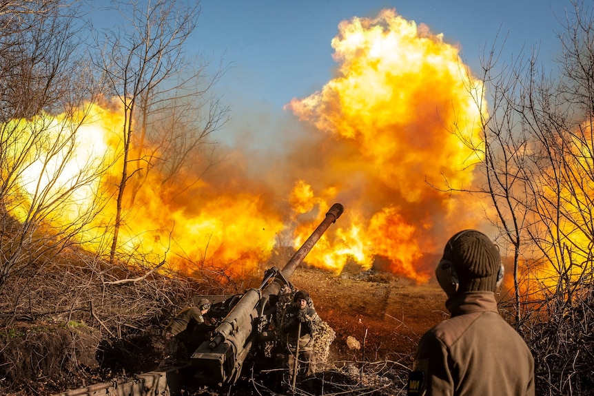 Large flames in bush scrub behind a field gun and a person in army colours