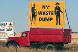 A yellow 'no nuclear waste dump' sign stands atop a red truck