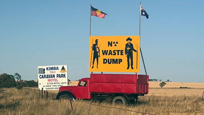 A yellow 'no nuclear waste dump' sign stands atop a red truck